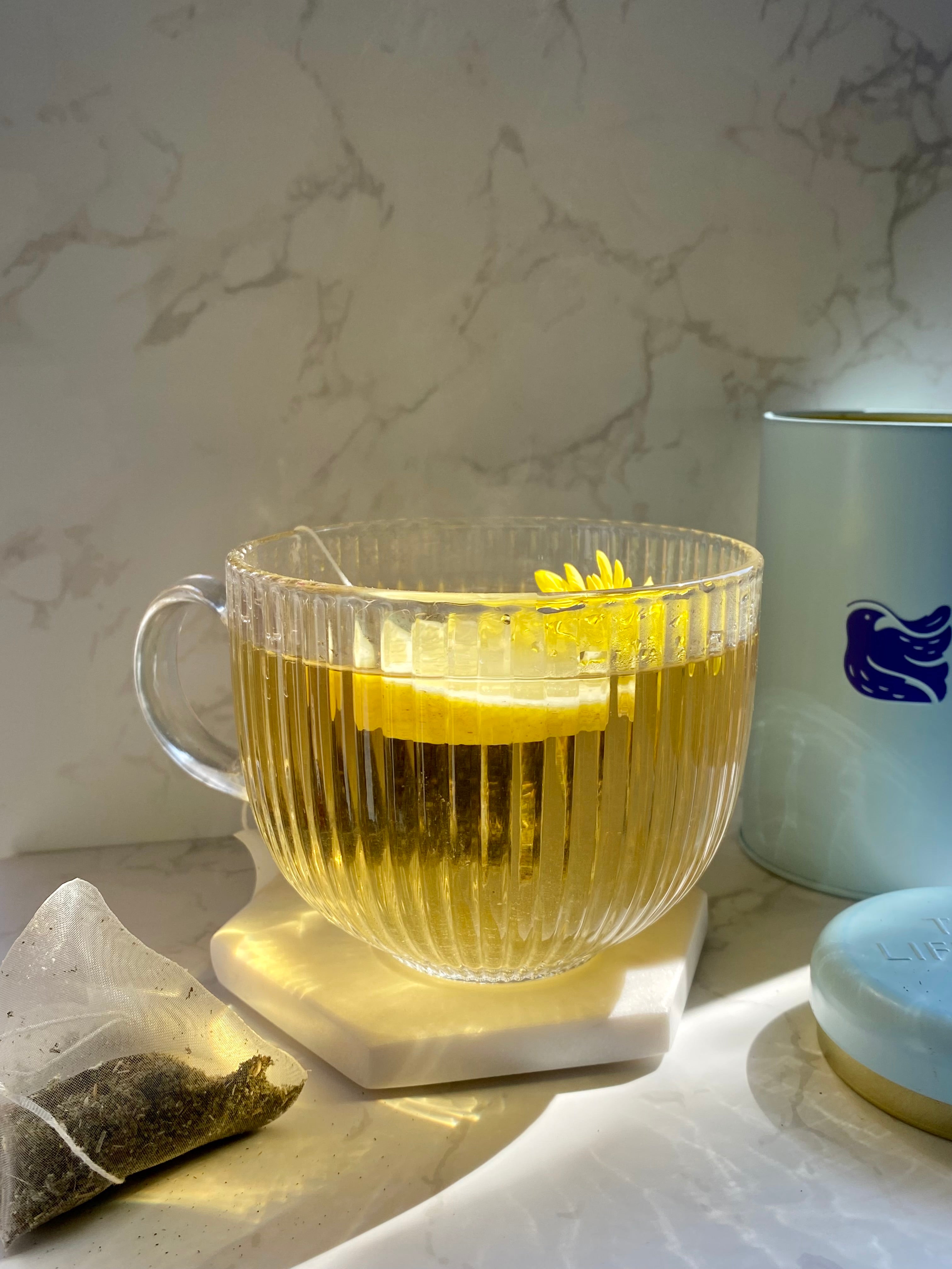 Cup of tea with lemon slice next to it and a tin of TLC tea with it