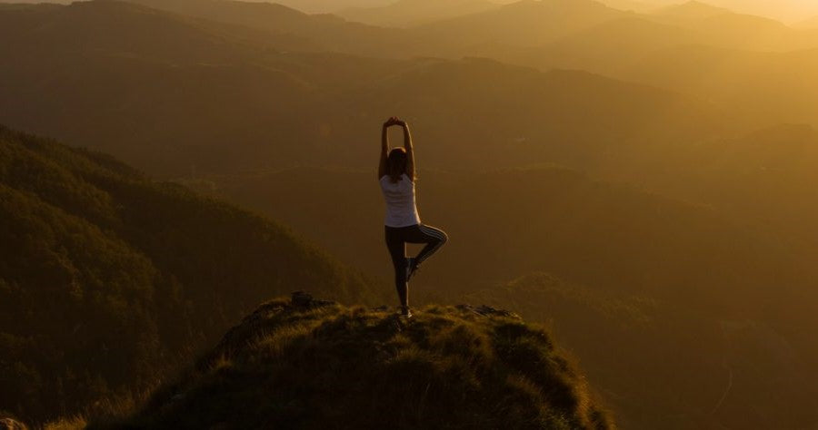 Woman in yoga pose while looking at the sun going down